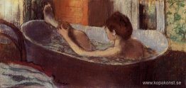 Kvinna i ett bad som svampar hennes ben Kvinna i ett bad som svampar hennes ben